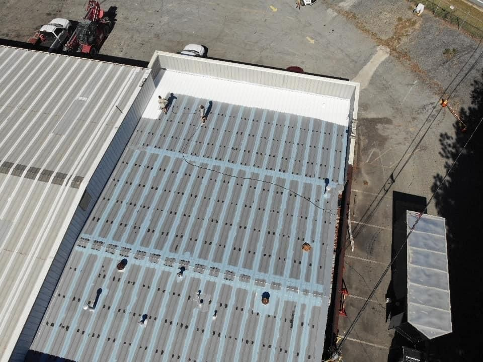 Aerial view of a corrugated metal roof with white trim. Workers are visible on the roof.