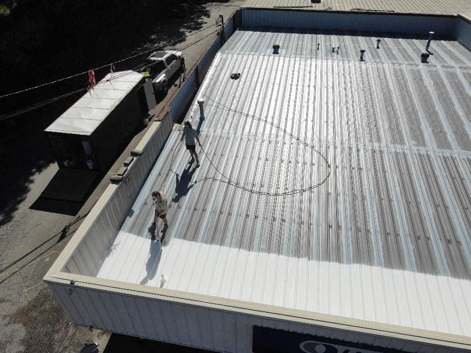 Two people working on a large metal roof of a building. Grey metal with white edges, truck on the side.