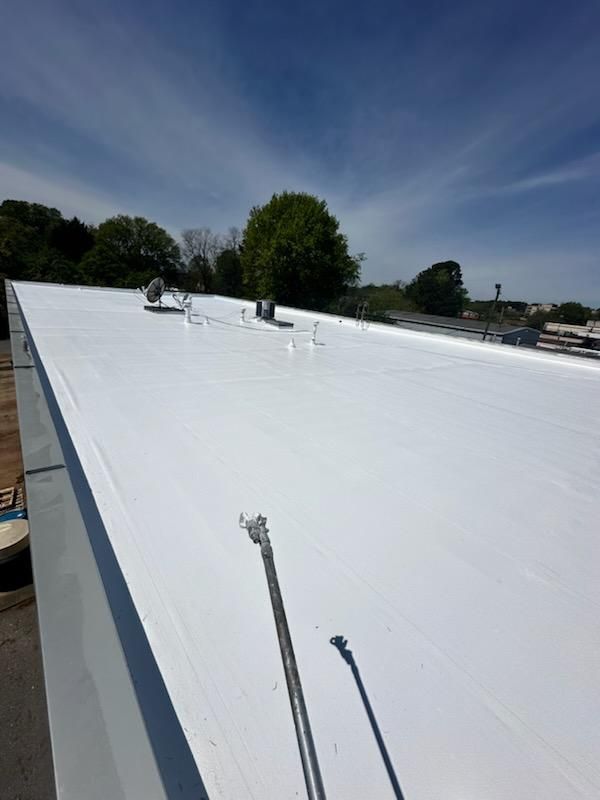 White roof on a building under a bright blue sky with trees in the distance.
