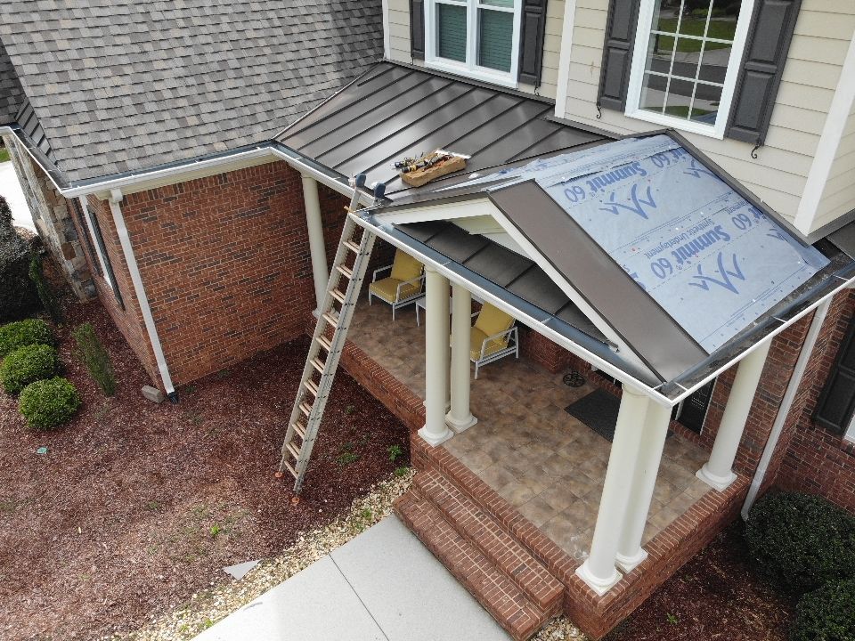 House with metal roofing and brick porch. Ladder against porch roof. Brown and beige exterior.
