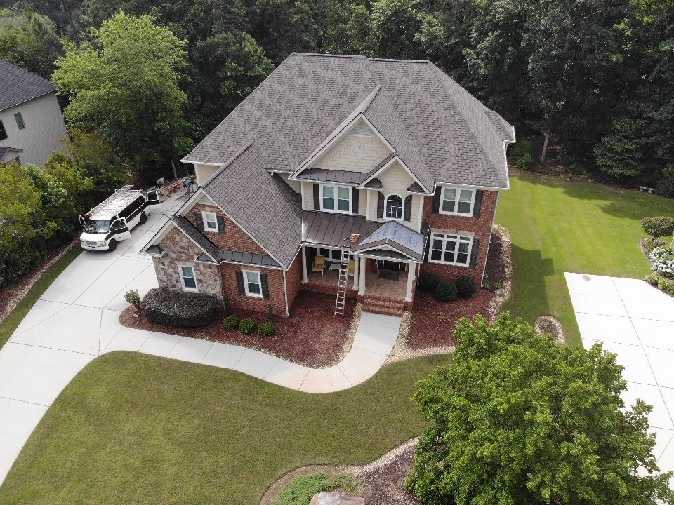 Aerial view of a two-story brick home with a gray roof and a well-manicured lawn and a vehicle in the driveway.